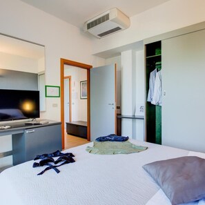 Una habitación de hotel con una cama, un escritorio con una computadora, un televisor y un armario.