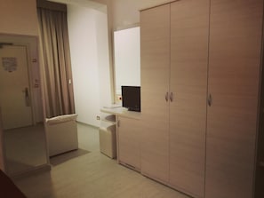 Une chambre d’hôtel avec une armoire en bois, un petit bureau avec une télévision et une table de chevet.