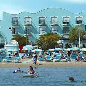 Un hôtel situé en bord de mer, doté de nombreux balcons, de chaises de plage et de parasols.