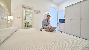 Een hotelkamer met een bed, een laptop, een nachtkastje, een kledingkast en een badkamer die door een open deur zichtbaar is.