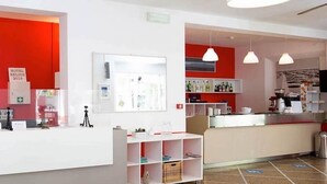 Un hall d’hôtel avec un mur rouge, un comptoir d’accueil, une horloge et un écran de télévision.