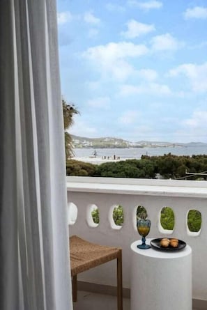 A balcony with a view of the sea, a table with a glass of juice and pastries, and a chair. - Galation Hotel Mykonos (Mykonos)