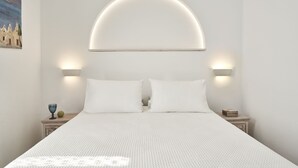 A bed with a white textured bedspread, two white pillows, and a headboard with a semi-circular light fixture. - Galation Hotel Mykonos (Mykonos)