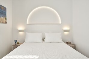 A bed with a white textured bedspread, two white pillows, and a headboard with a semi-circular light fixture. - Galation Hotel Mykonos (Mykonos)