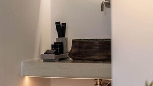 A bathroom with a white sink, a mirror, a towel, and a wooden shelf. - Galation Hotel Mykonos (Mykonos)