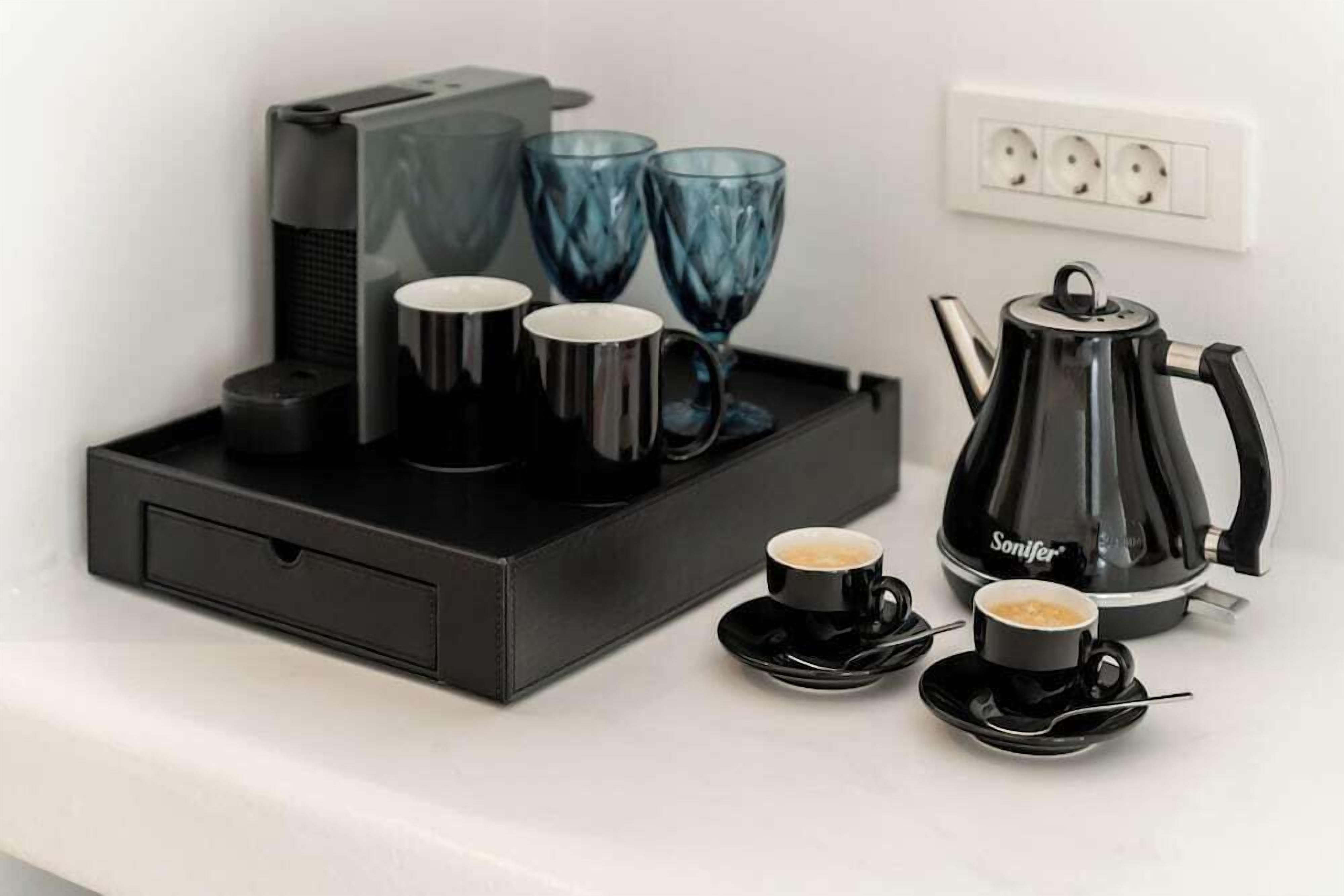 Une machine à café, deux verres bleus et deux tasses noires sur un plateau.