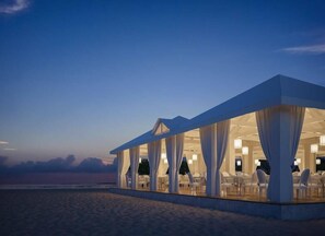 A beachside restaurant with a covered outdoor seating area, white curtains, and tables. - Sandies Bathala Maldives (Bathala Island)