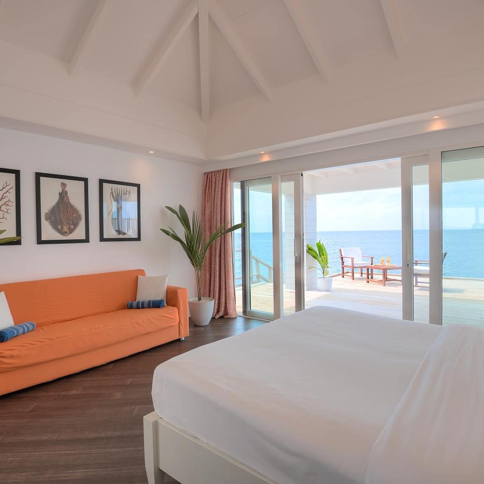 A hotel room with a bed, an orange sofa, a large window, and a view of the sea.