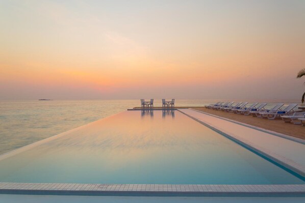 A infinity pool with lounge chairs and tables, overlooking the sea at sunset. - Sandies Bathala Maldives (Bathala Island)