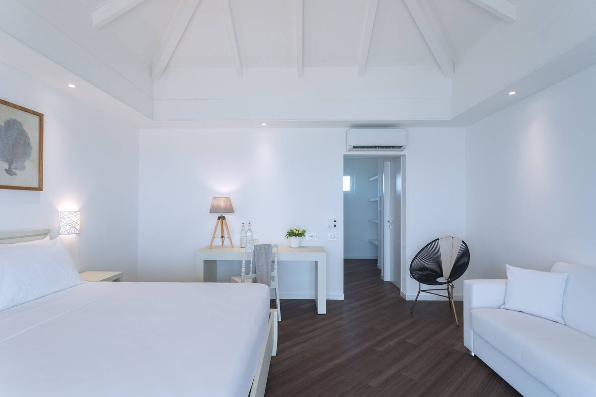 Une chambre d’hôtel équipée d’un lit, d’un bureau, d’une chaise, d’un ventilateur et d’une porte donnant sur une autre pièce.