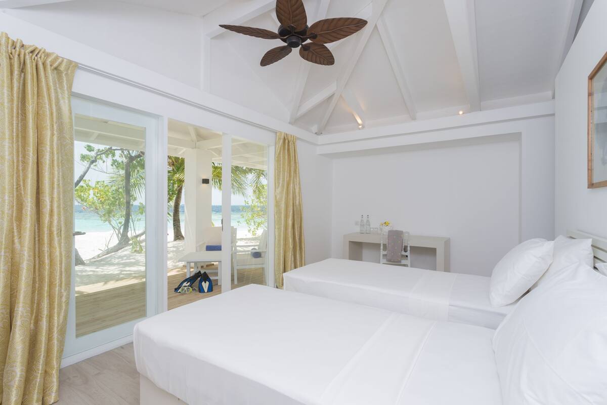 Une chambre avec deux lits, un ventilateur de plafond, une table de chevet et une vue sur la plage.