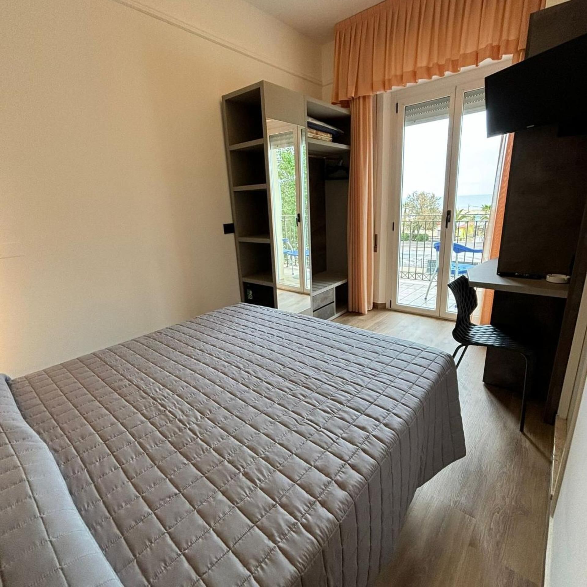Een slaapkamer met een bed, een televisie, een kledingkast en een balkon met uitzicht.