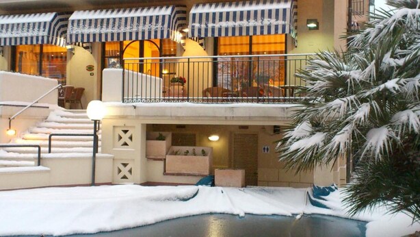 Ein Hotel mit Pool, Außenbereich mit Sitzgelegenheiten und überdachter Liegefläche mit Sonnenschirmen.