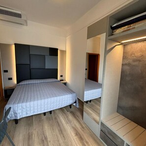 A bedroom with a bed, bedside tables, a mirror, and a built-in wardrobe. - Cobalto (Rimini)