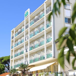 A multi-story hotel with a prominent sign, balconies with glass railings, and a clear sky. - Hotel Parco (Riccione)