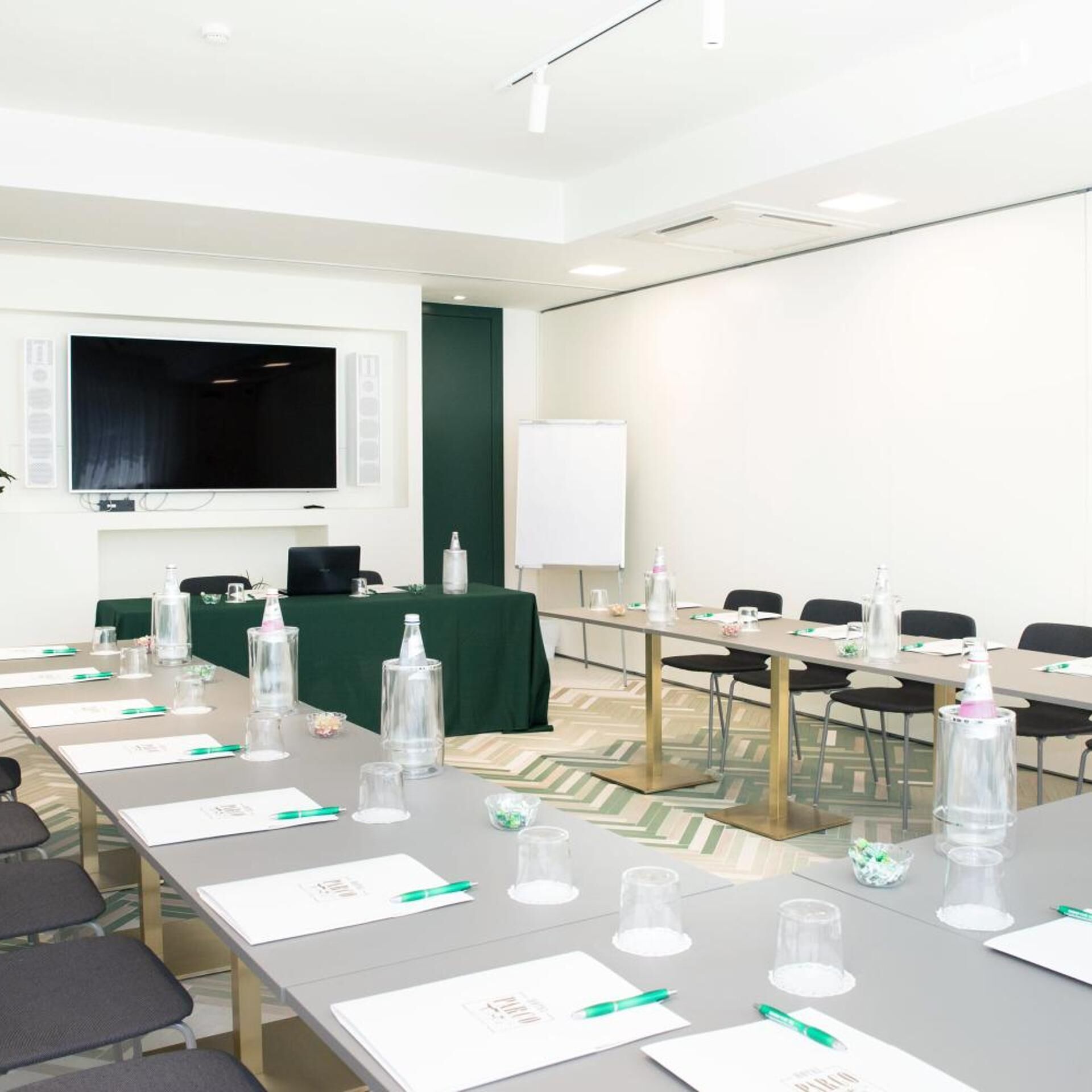 Ein Konferenzraum mit langem Tisch, Stühlen, einer Whiteboard und einem Fernsehbildschirm.
