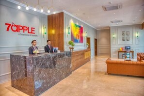 A hotel reception area with a marble counter, two receptionists, a colorful mural, and a plush sofa. - 7 Apple Hotel Vimannagar, Pune (Pune)