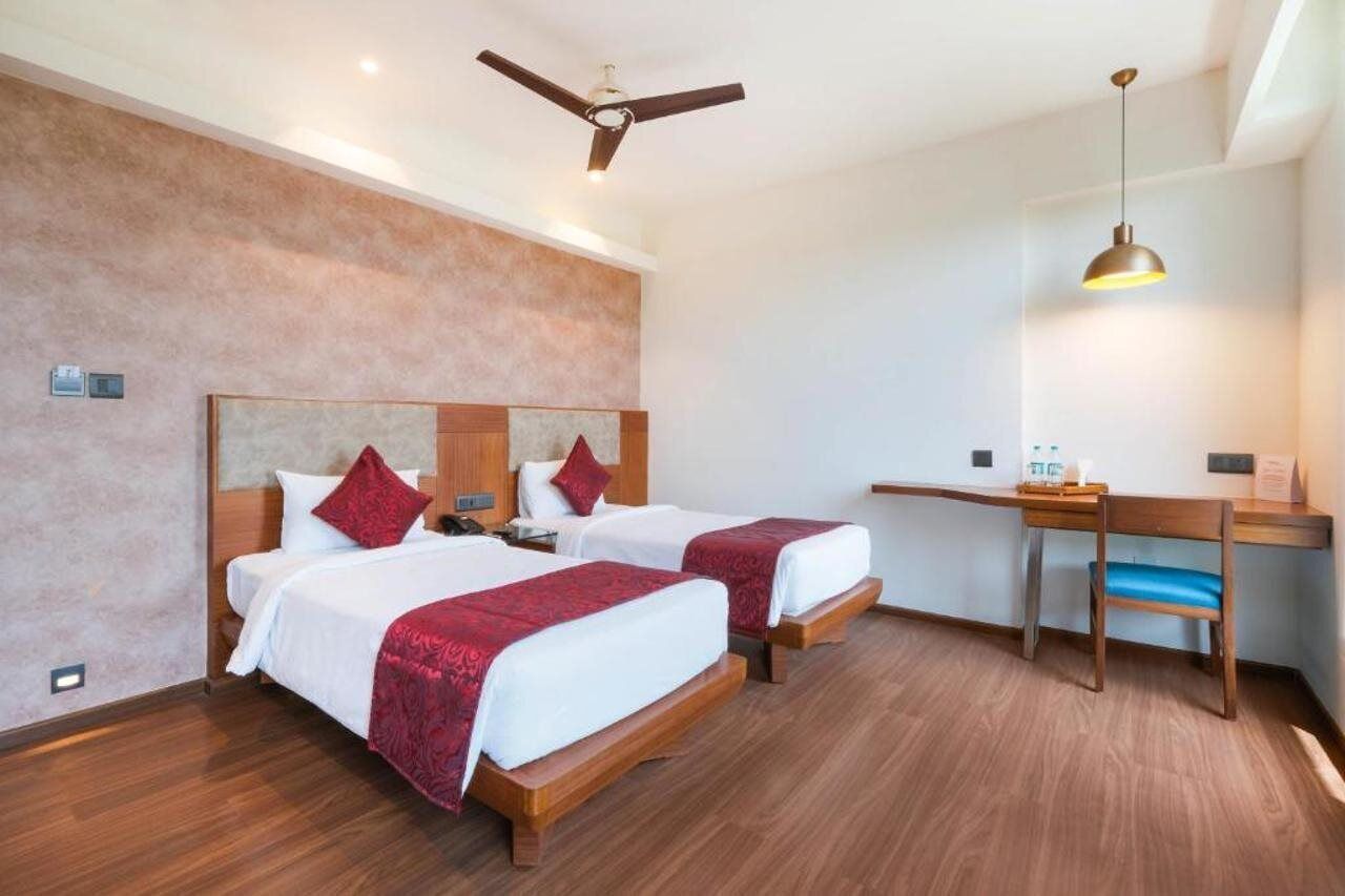 A hotel room with two beds, a desk, a chair, a ceiling fan, and a pendant light.