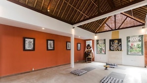 A spacious room with a high ceiling, framed artwork on the walls, and a central statue. - Nawa Sakti Resort (Ubud)