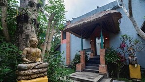 A serene outdoor area with a Buddha statue, a thatched-roof structure, and a staircase leading to a building. - Nawa Sakti Resort (Ubud)