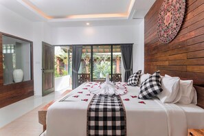 A bedroom with a large bed, a wooden headboard, a decorative wall piece, and a view of the outdoors through a glass door. - Nawa Sakti Resort (Ubud)
