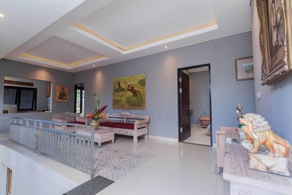 A spacious living area with a high ceiling, a sofa set, a decorative lion statue, and a painting on the wall.