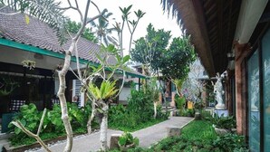 A courtyard with a pathway, various plants, and a building with a tiled roof. - Nawa Sakti Resort (Ubud)