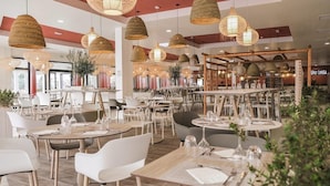 Un restaurante moderno con mesas redondas, sillas blancas e iluminación colgante tejida.