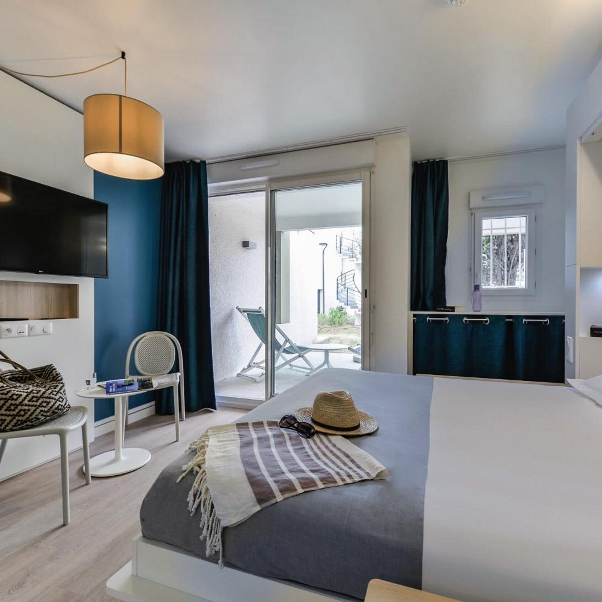 A modern hotel room with a bed, a television, a chair, a table, and a view of the outside.