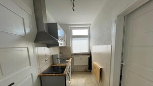 Een smalle keuken met een ingebouwde oven, een raam en een radiator.