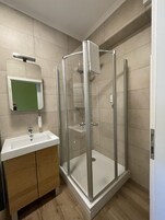 Un baño moderno con ducha envuelta en vidrio, lavamanos con espejo y armarios de madera.