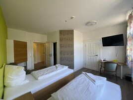 Habitación de hotel con dos camas, un escritorio con silla, un televisor montado en la pared y una puerta que da a otra habitación.