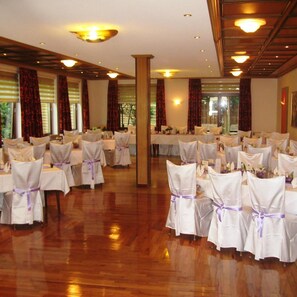 Une salle de banquet avec des tables rondes, des nappes blanches et des chaises ornées de rubans violets.