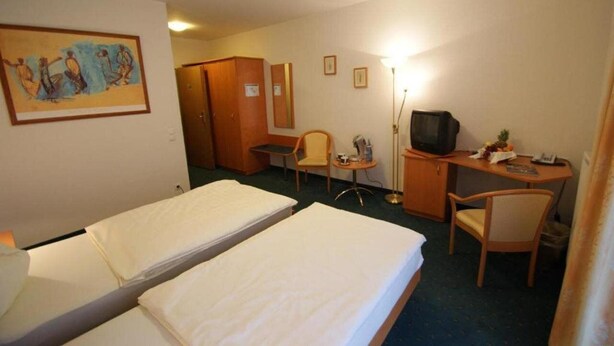 A hotel room with two single beds, a desk with a chair, a television, and a small table with a lamp. - Wald-cafe Landhotel Restaurant (Bonn)