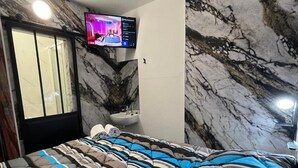 A bedroom with a bed, a television mounted on the wall, a toilet, and a marble-patterned wall. - Hotel Classeco Gent (Ghent)