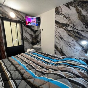 A bedroom with a bed, a television mounted on the wall, a toilet, and a marble-patterned wall. - Hotel Classeco Gent (Ghent)