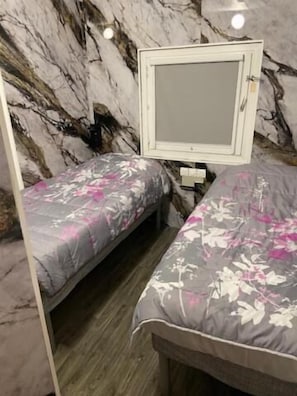 A bedroom with two beds, a marble-patterned wall, and a white-framed mirror.