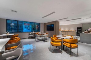 A modern interior with a dining area featuring round tables and orange chairs, a large window with a view, and a kitchen area with a counter. - Borrman Hotel (Guangzhou)