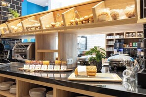 Ein Frühstücksbuffet mit verschiedenen Backwaren, Aufstrichen, einer Kaffeemaschine und einer Pflanze.
