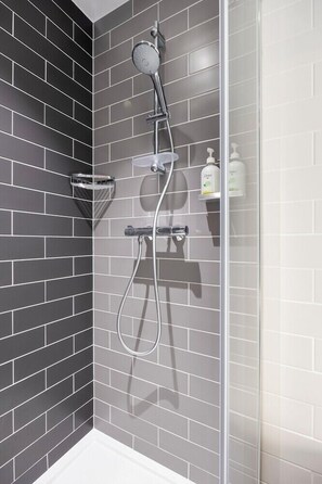 Une douche moderne avec un pare-douche en verre, des carreaux gris et un pommeau de douche à main.