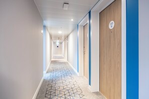 Un pasillo con alfombra de estampado geométrico, una puerta de madera con placa de número y una pared de acento azul.