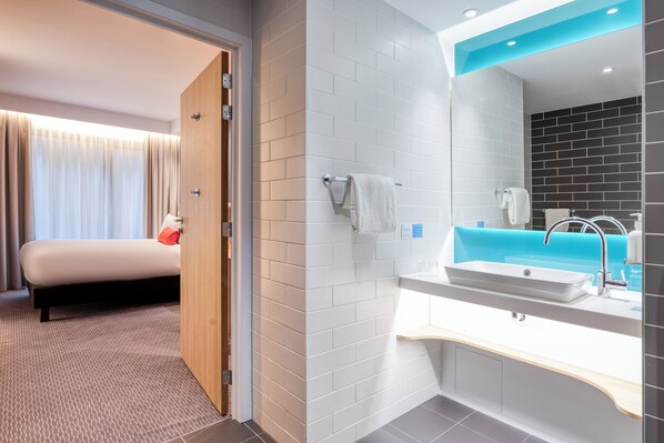 Une chambre d’hôtel moderne, équipée d’un lit, d’une salle de bain avec un lavabo et un miroir, et offrant une vue sur l’extérieur.