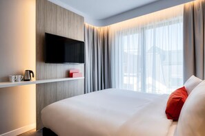 Une chambre d’hôtel équipée d’un lit, d’un téléviseur fixé au mur, d’une machine à café et d’une fenêtre avec des rideaux.