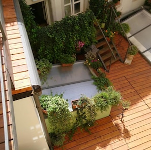 Um jardim no terraço com deck de madeira, vasos de plantas e escada de metal.
