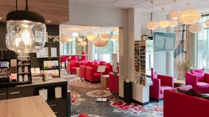 Eine Hotelhalle mit roten Sitzgelegenheiten, einer Kaffeebar und einem großen Fernseher.