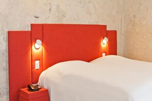 Ein Hotelzimmer mit rotem Kopfteil, Nachttischlampen, einem Telefon und einer weißen Bettdecke.