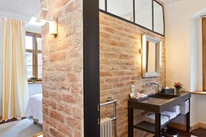 A modern bathroom with a brick wall, a large mirror, a dark sink, and a towel rack. - Hotel David (Regensburg)