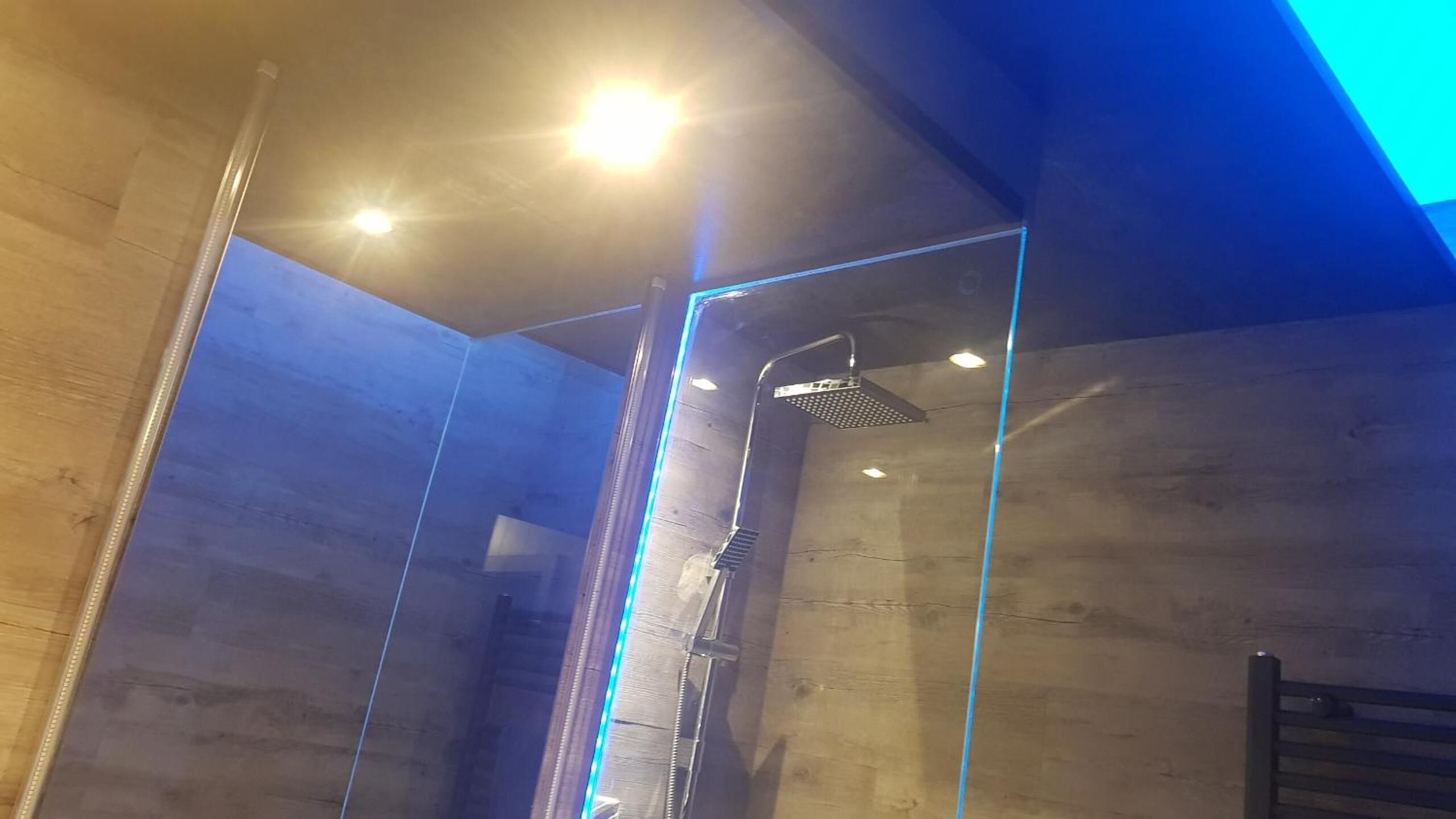 Ein modernes Badezimmer mit Duschkabine aus Glas, einer sichtbaren Dusche und Einbauleuchten.