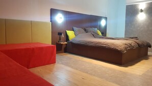 A modern bedroom with a large bed, a red ottoman, and a nightstand with a lamp. - Modern Hoteliving Giessen (Pohlheim)