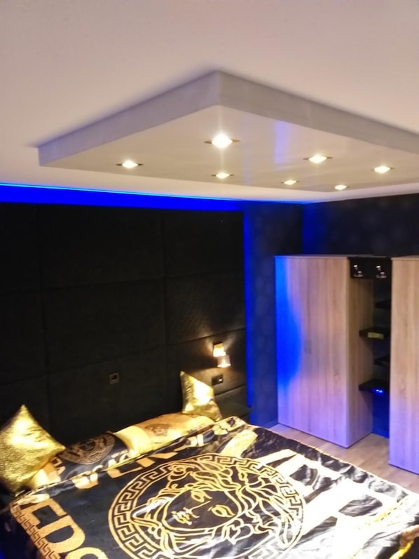 Un dormitorio moderno con una cama grande, paredes oscuras y detalles de iluminación azul.